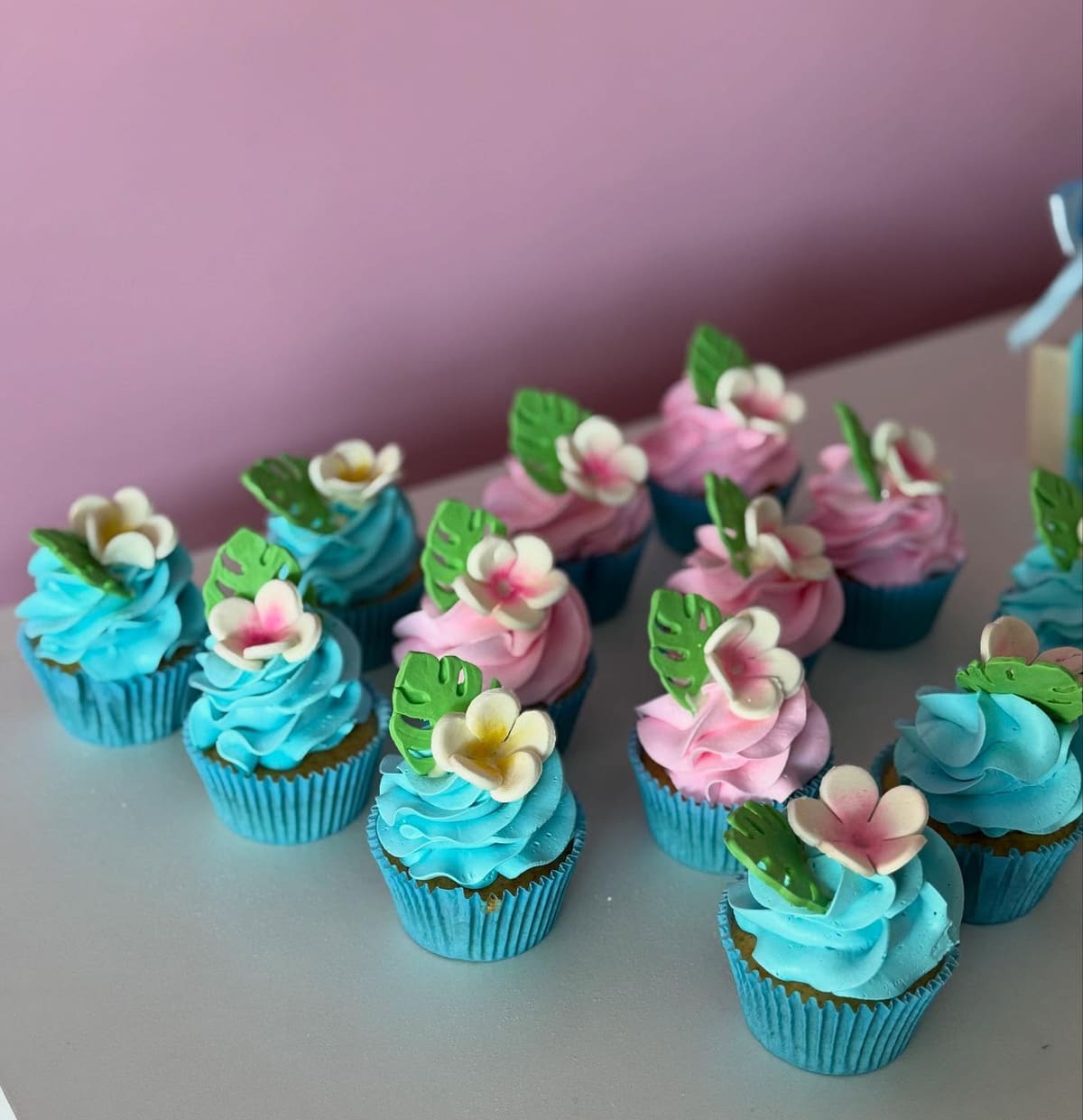 Cupcakes com cobertura azul e rosa decorados com flores e folhas de açúcar